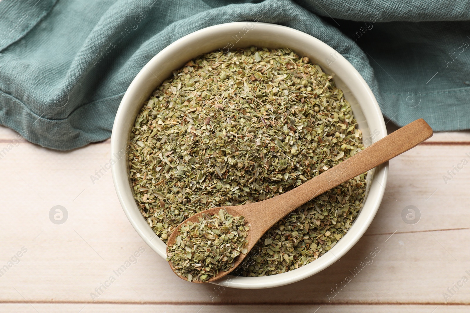 Photo of Dried oregano in bowl and spoon on wooden table, top view