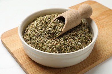 Photo of Dried oregano in bowl and scoop on white table, closeup