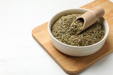 Dried oregano in bowl and scoop on white table, closeup