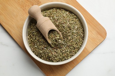 Photo of Dried oregano in bowl and scoop on white marble table, top view