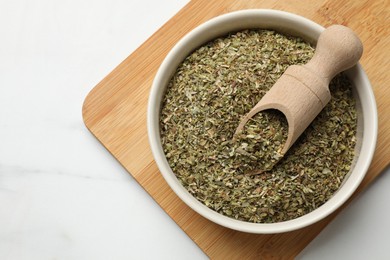 Photo of Dried oregano in bowl and scoop on white marble table, top view