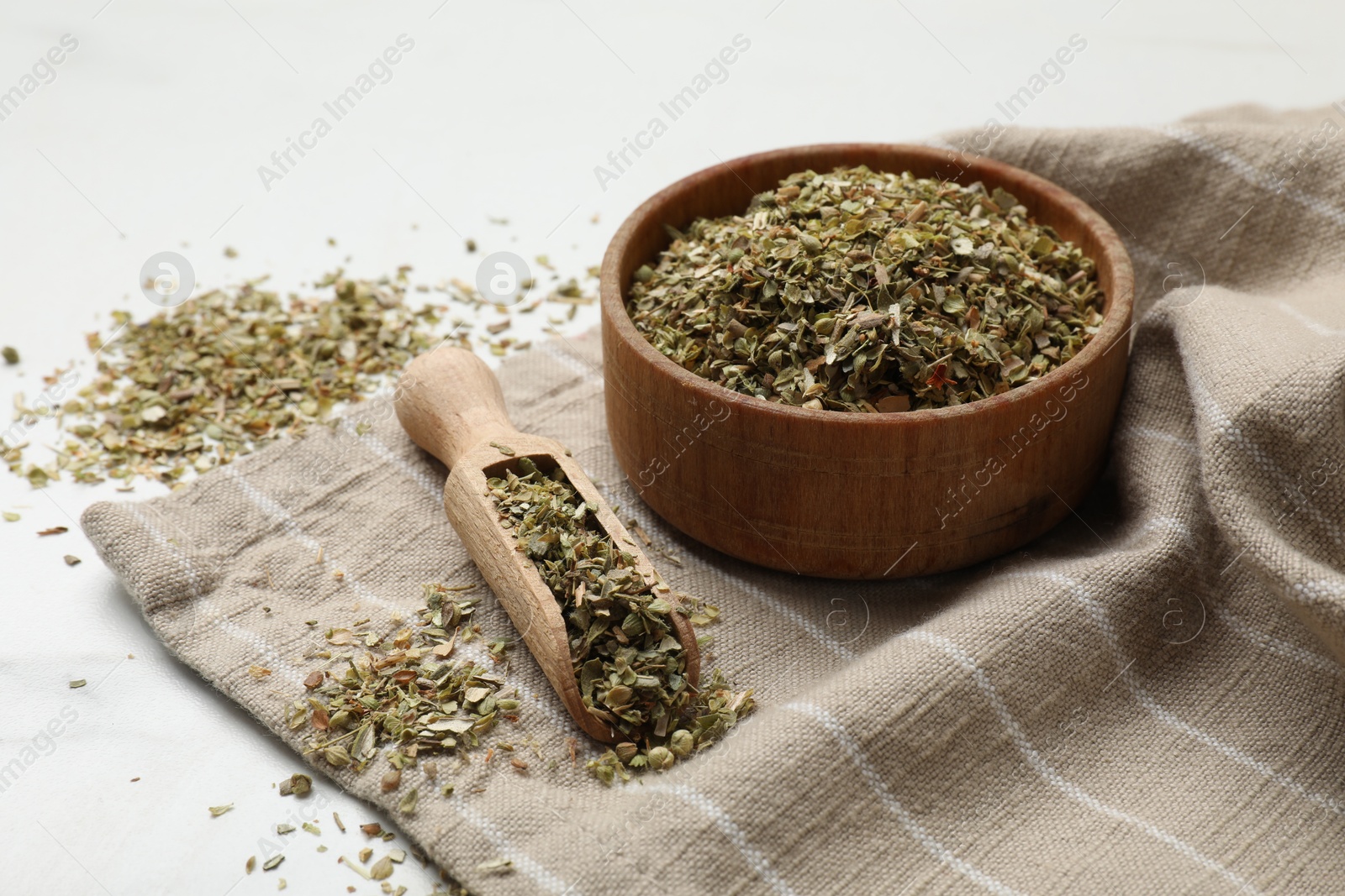 Photo of Dried oregano in bowl and scoop on white table