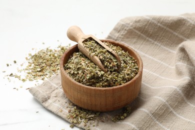 Photo of Dried oregano in bowl and scoop on white table, closeup