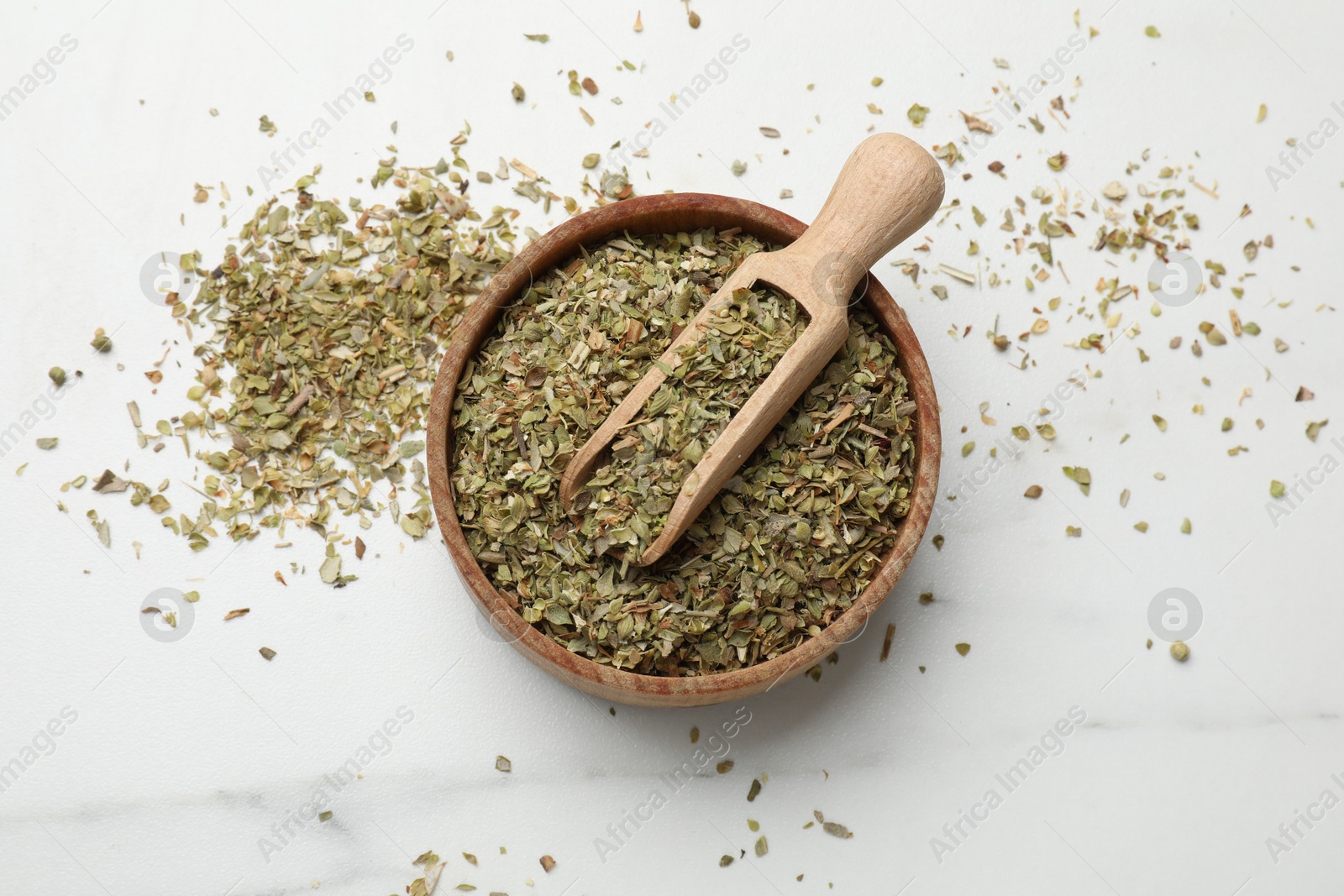 Photo of Dried oregano in bowl and scoop on white marble table, top view