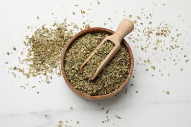 Photo of Dried oregano in bowl and scoop on white marble table, top view