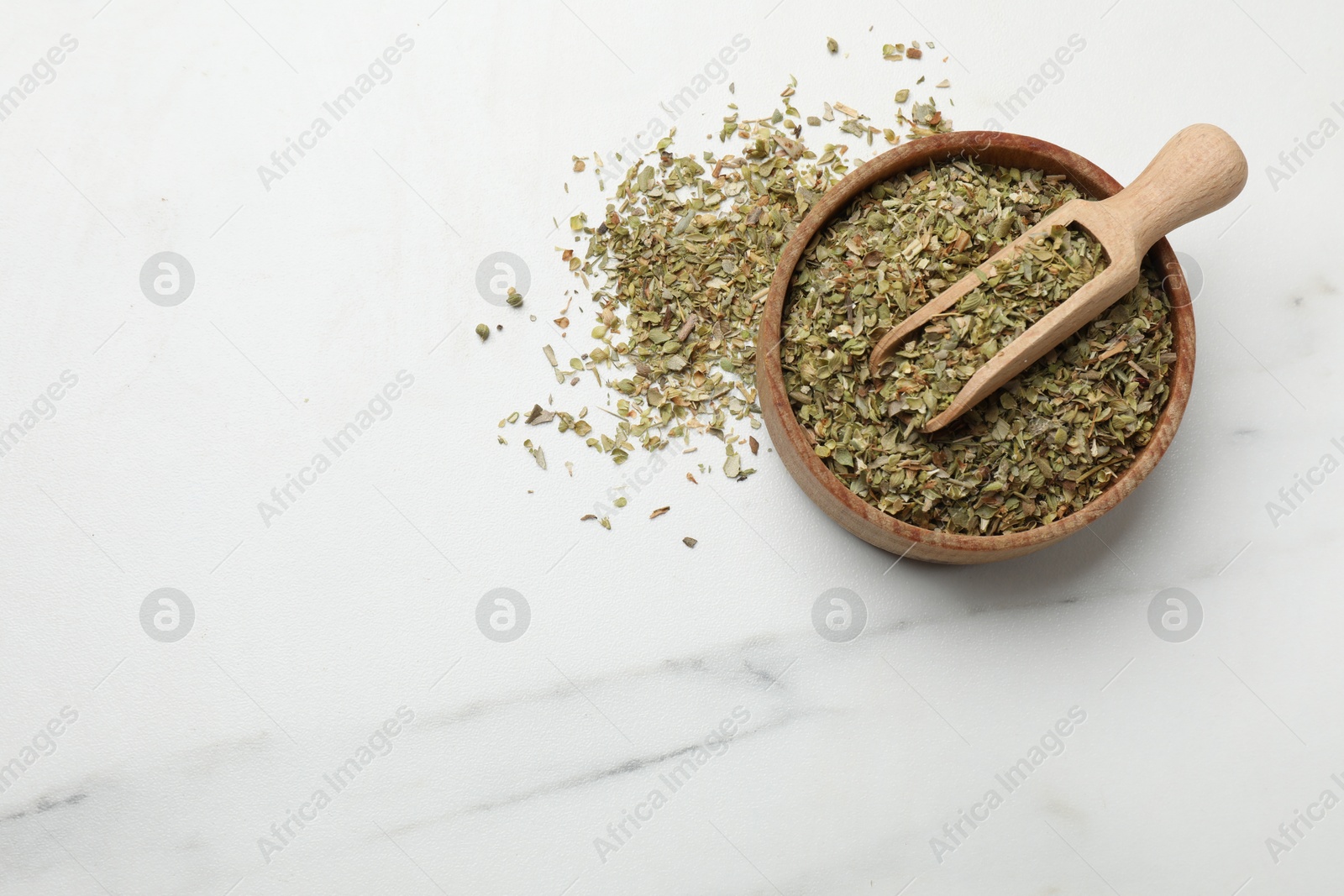 Photo of Dried oregano in bowl and scoop on white marble table, top view. Space for text