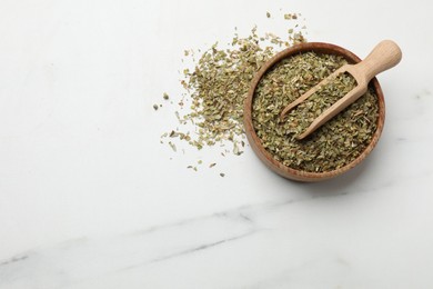 Photo of Dried oregano in bowl and scoop on white marble table, top view. Space for text