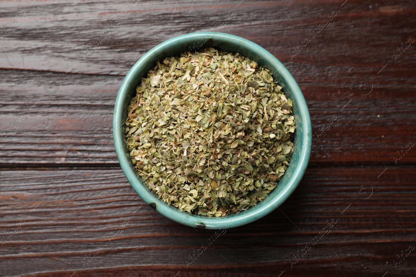 Photo of Dried oregano in bowl on wooden table, top view