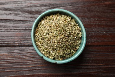 Dried oregano in bowl on wooden table, top view