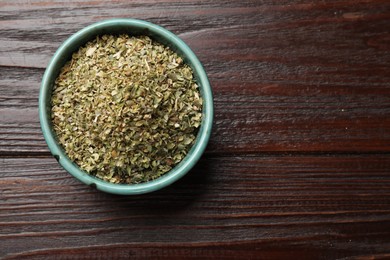 Photo of Dried oregano in bowl on wooden table, top view. Space for text