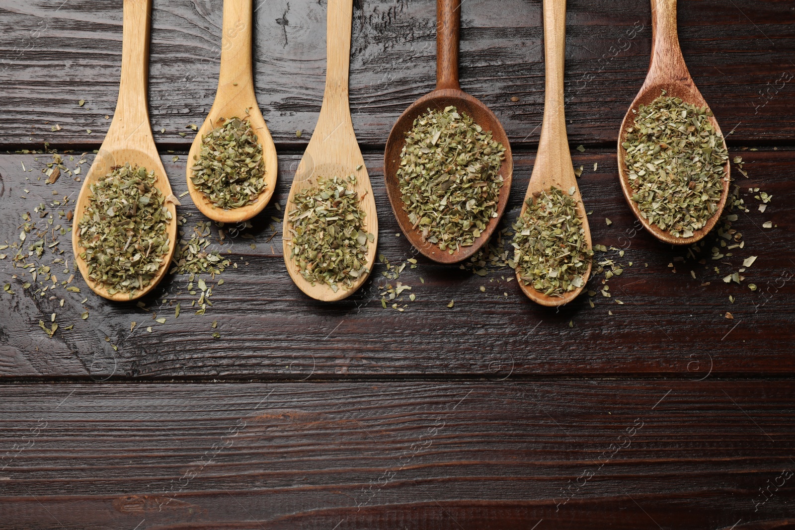 Photo of Dried oregano in spoons on wooden table, flat lay