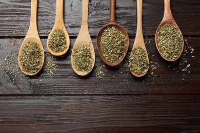 Dried oregano in spoons on wooden table, flat lay