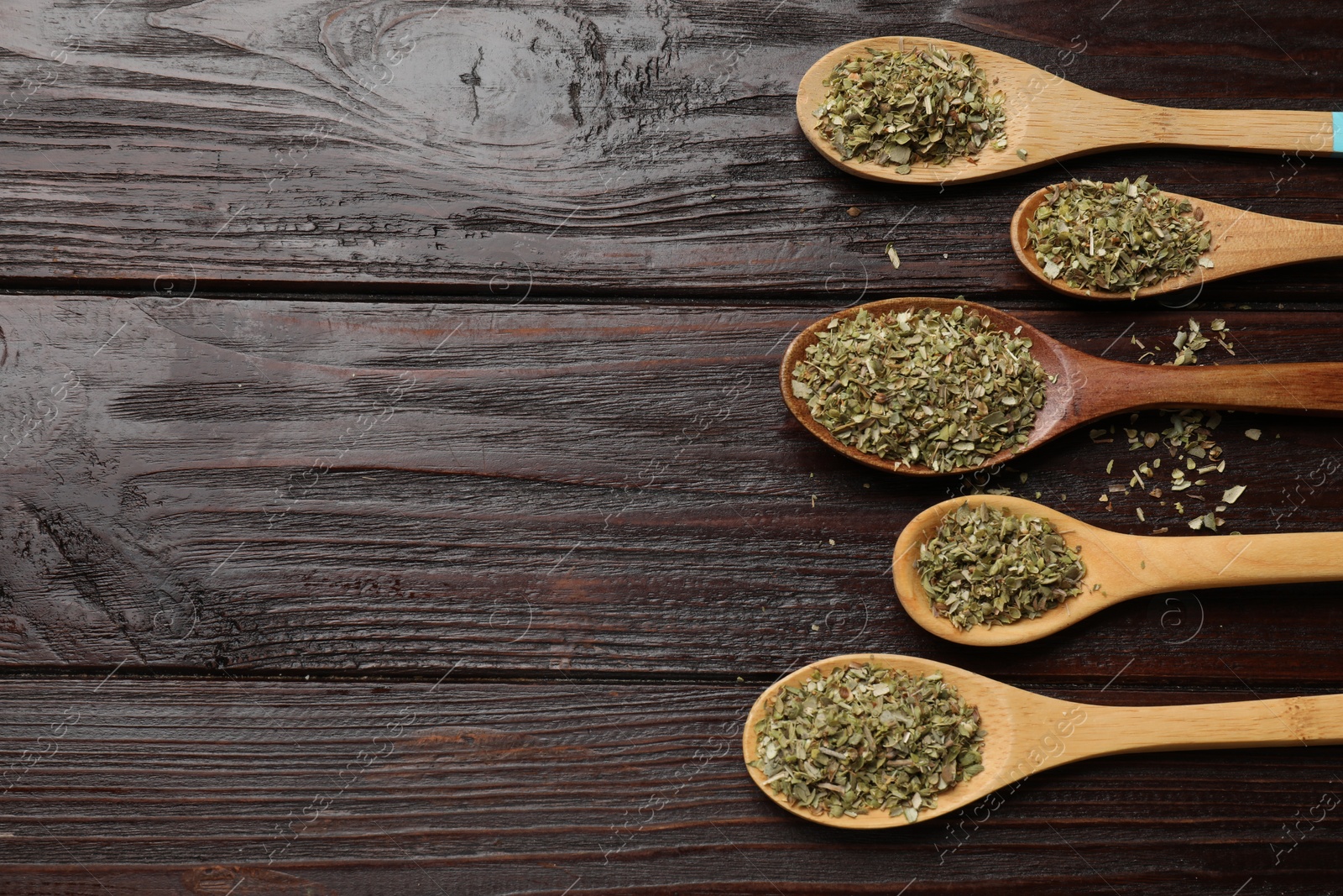 Photo of Dried oregano in spoons on wooden table, flat lay. Space for text