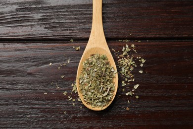 Dried oregano in spoon on wooden table, top view