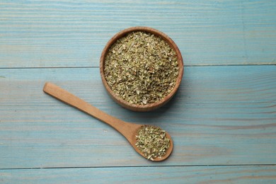 Photo of Dried oregano in bowl and spoon on light blue wooden table, top view