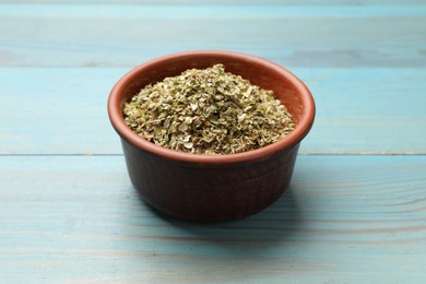 Photo of Dried oregano in bowl on light blue wooden table, closeup