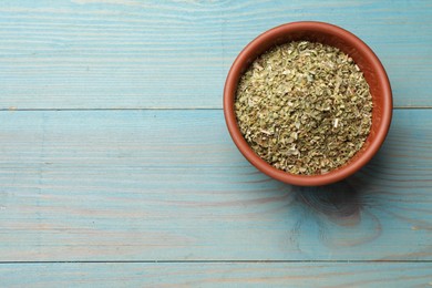 Dried oregano in bowl on light blue wooden table, top view. Space for text