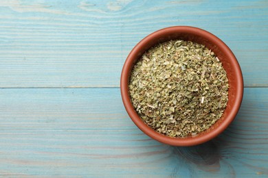 Dried oregano in bowl on light blue wooden table, top view. Space for text