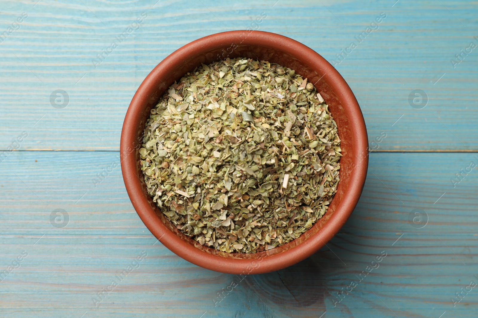 Photo of Dried oregano in bowl on light blue wooden table, top view