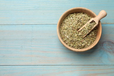 Photo of Dried oregano in bowl and scoop on light blue wooden table, top view. Space for text