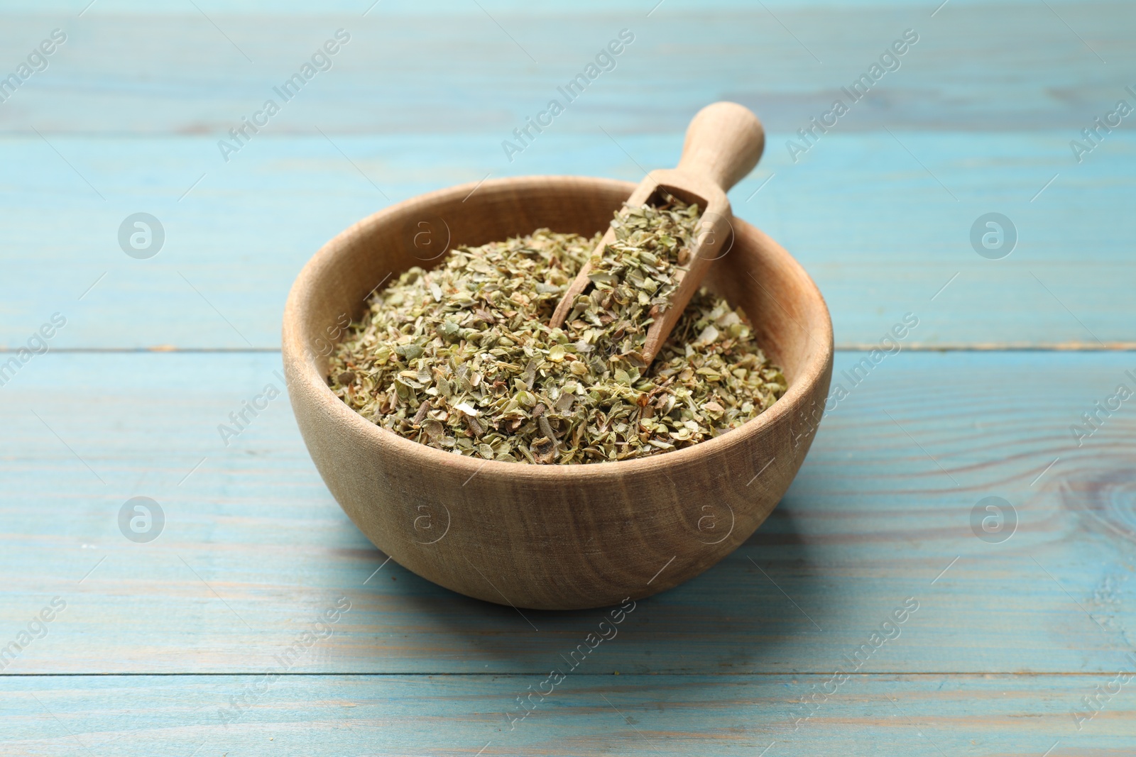 Photo of Dried oregano in bowl and scoop on light blue wooden table, closeup