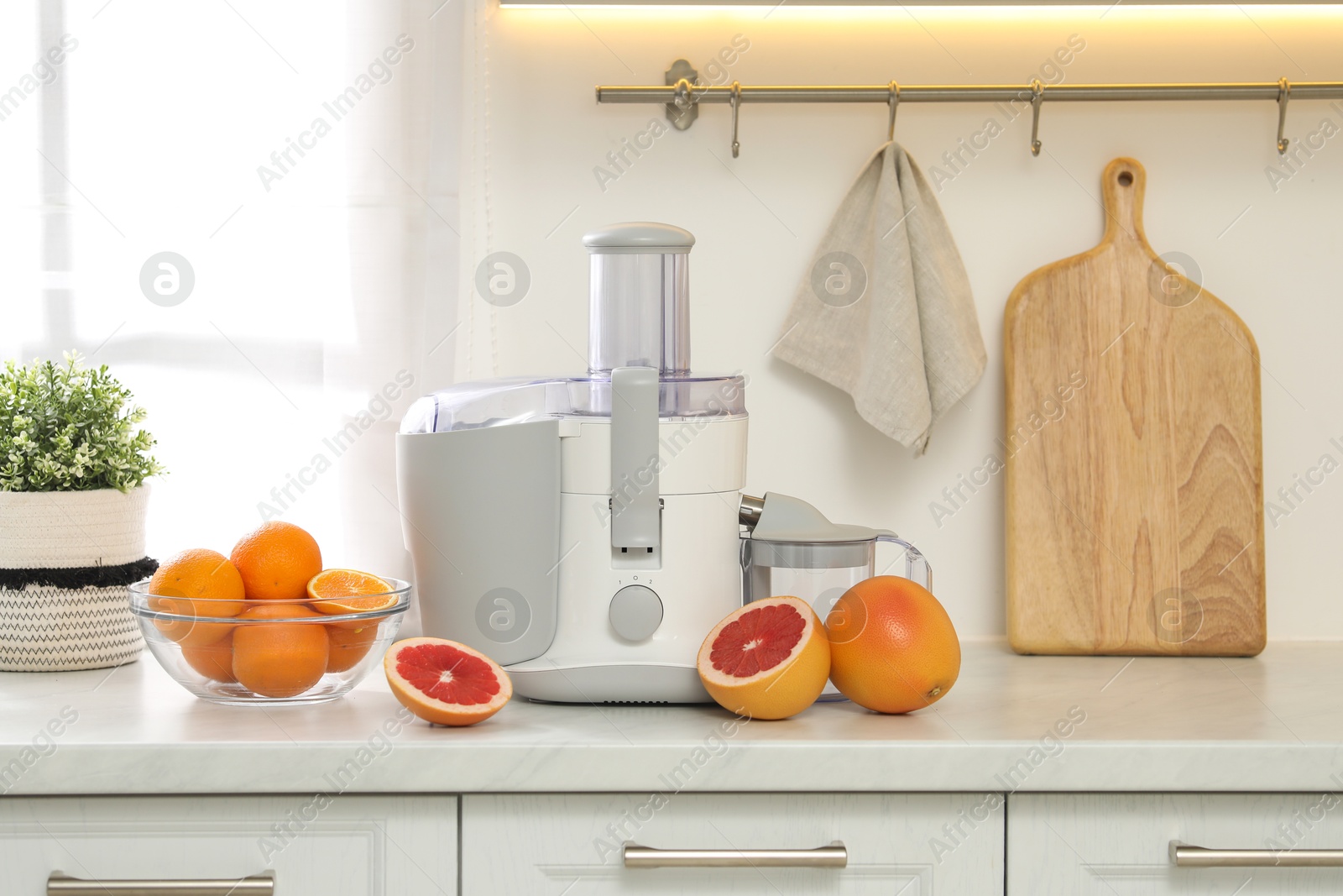 Photo of Modern juicer and grapefruits on white counter in kitchen