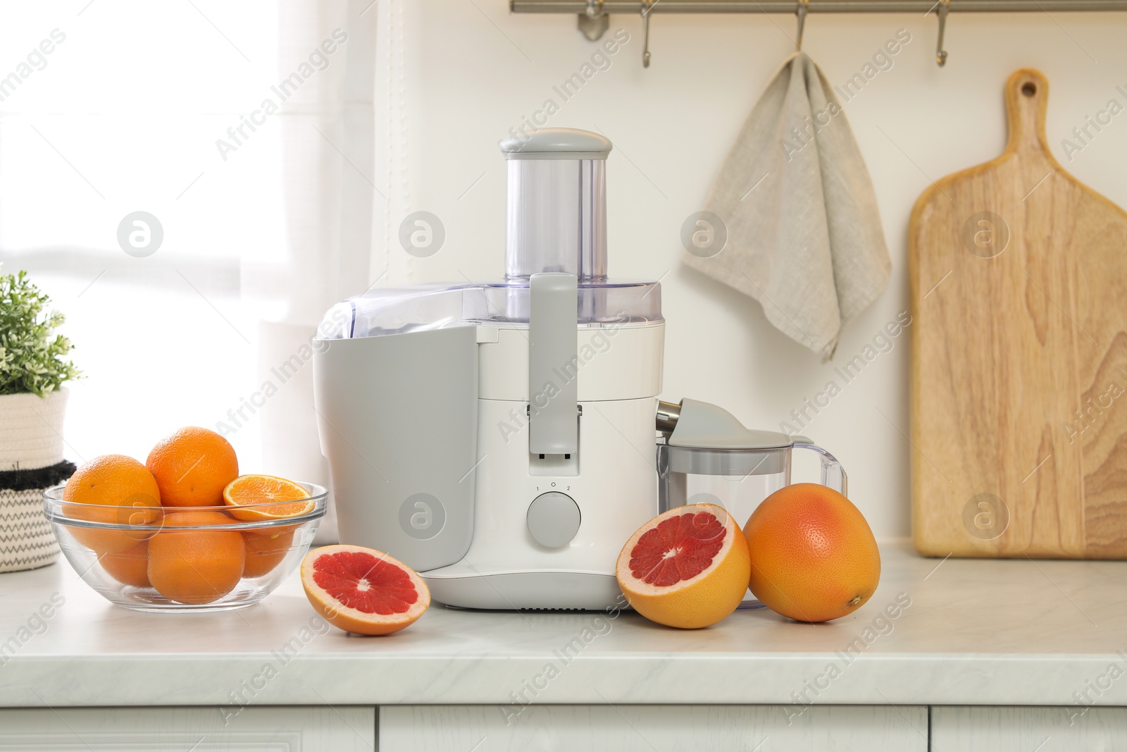 Photo of Modern juicer and grapefruits on white counter in kitchen