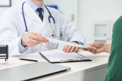 Photo of Doctor giving prescription to patient at white table in clinic, closeup