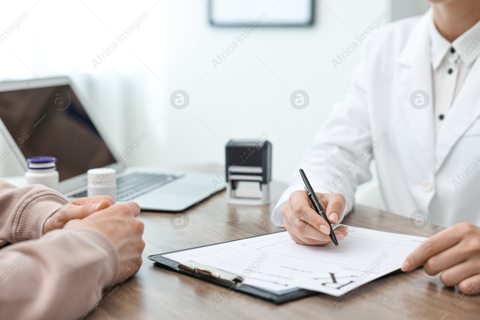 Photo of Doctor writing prescription for patient at wooden table in clinic, closeup