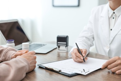 Photo of Doctor writing prescription for patient at wooden table in clinic, closeup