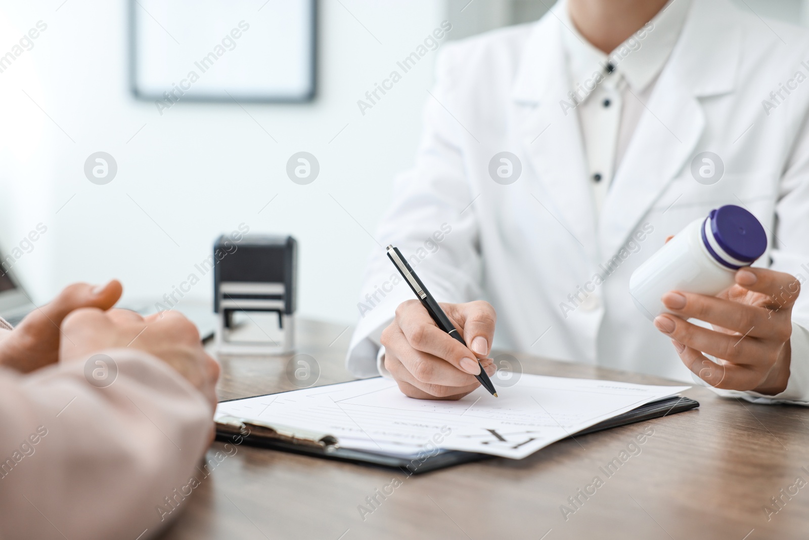 Photo of Doctor writing prescription for patient at wooden table in clinic, closeup