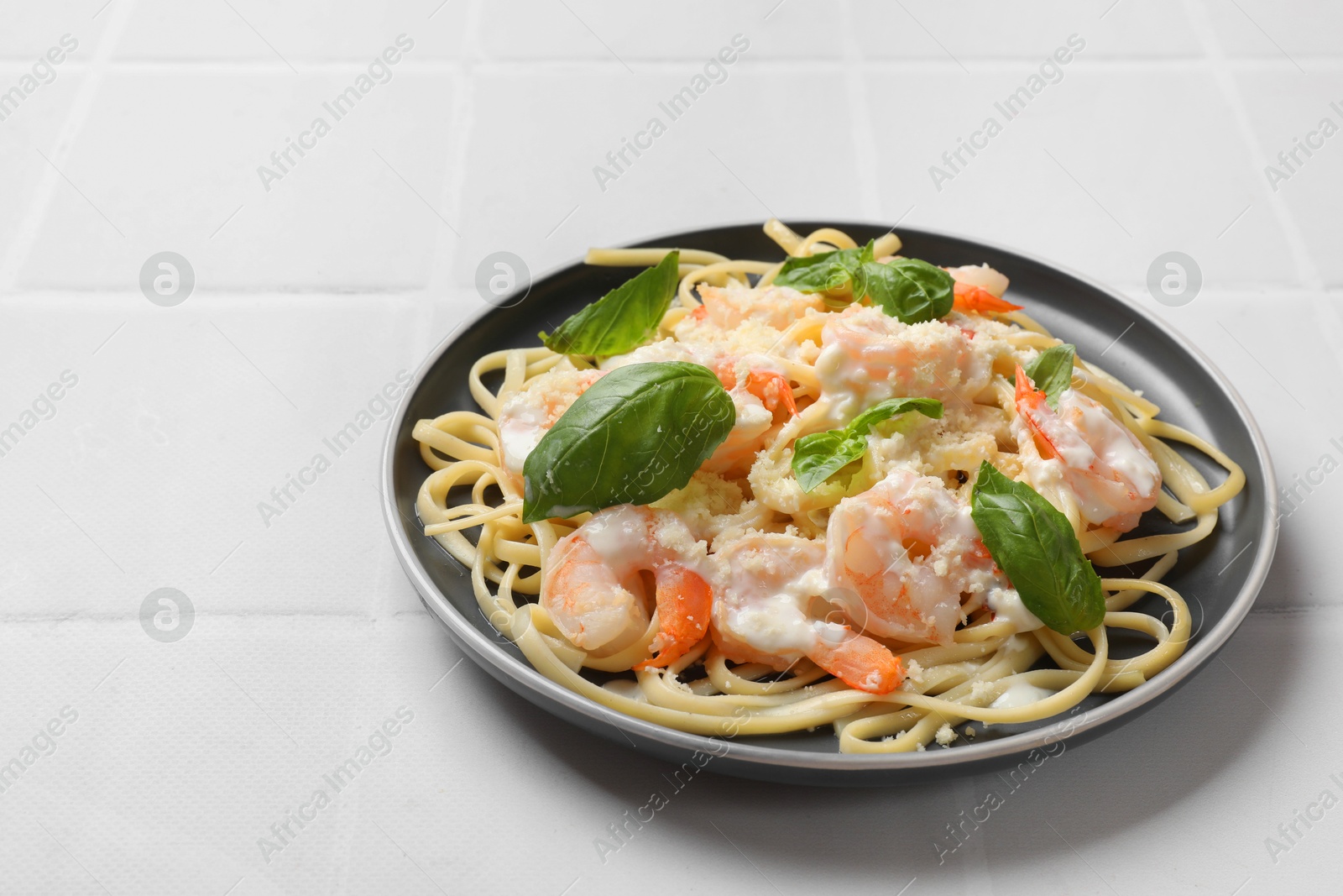 Photo of Tasty pasta with shrimps on white tiled table