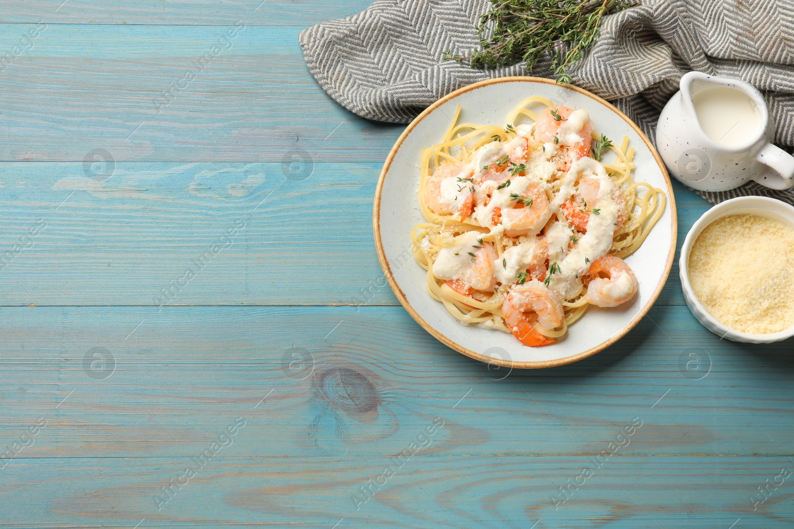 Photo of Tasty pasta with shrimps, creamy sauce and cheese on light blue wooden table, flat lay. Space for text