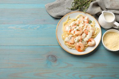 Photo of Tasty pasta with shrimps, creamy sauce and cheese on light blue wooden table, flat lay. Space for text