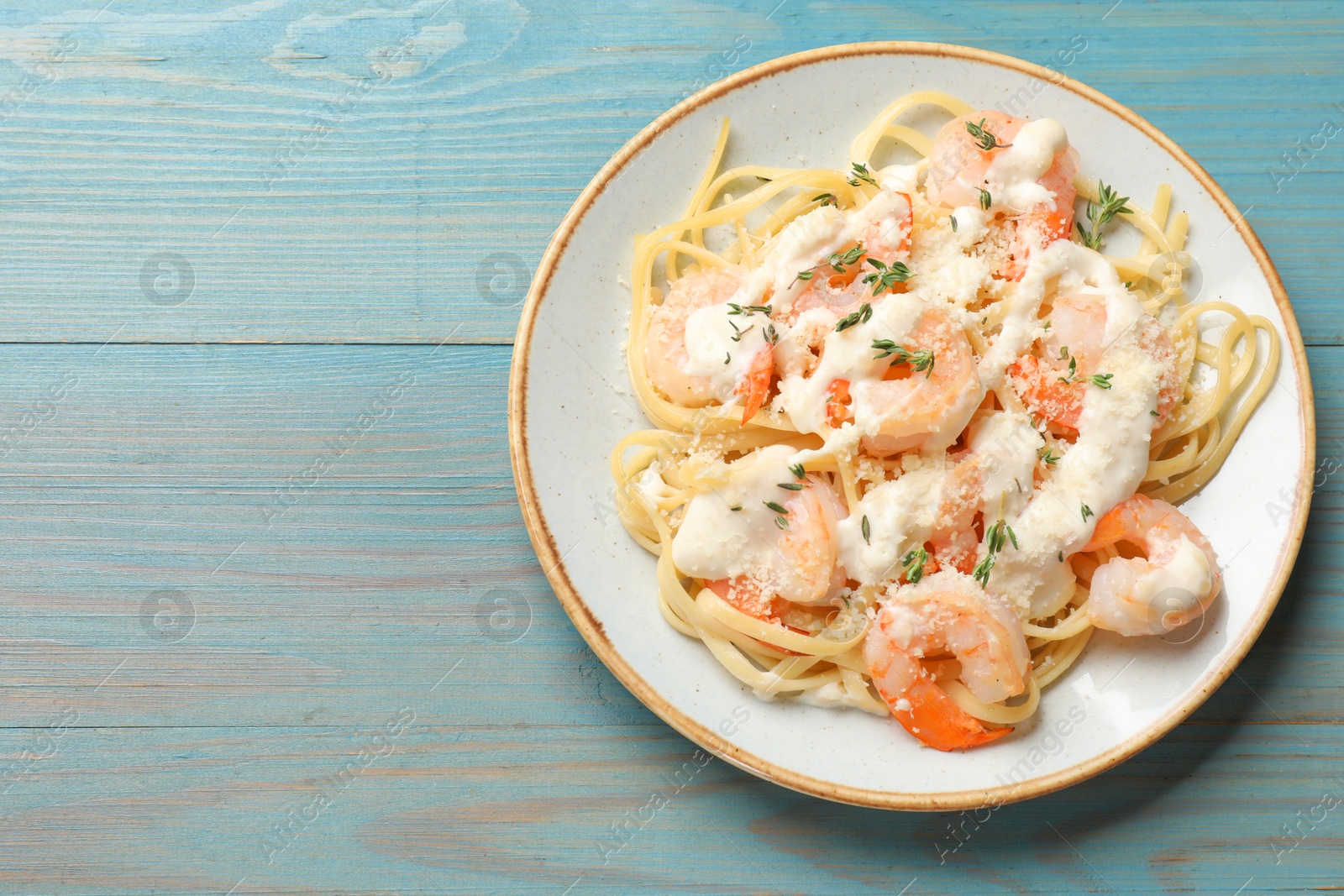 Photo of Tasty pasta with shrimps, creamy sauce and cheese on light blue wooden table, top view. Space for text