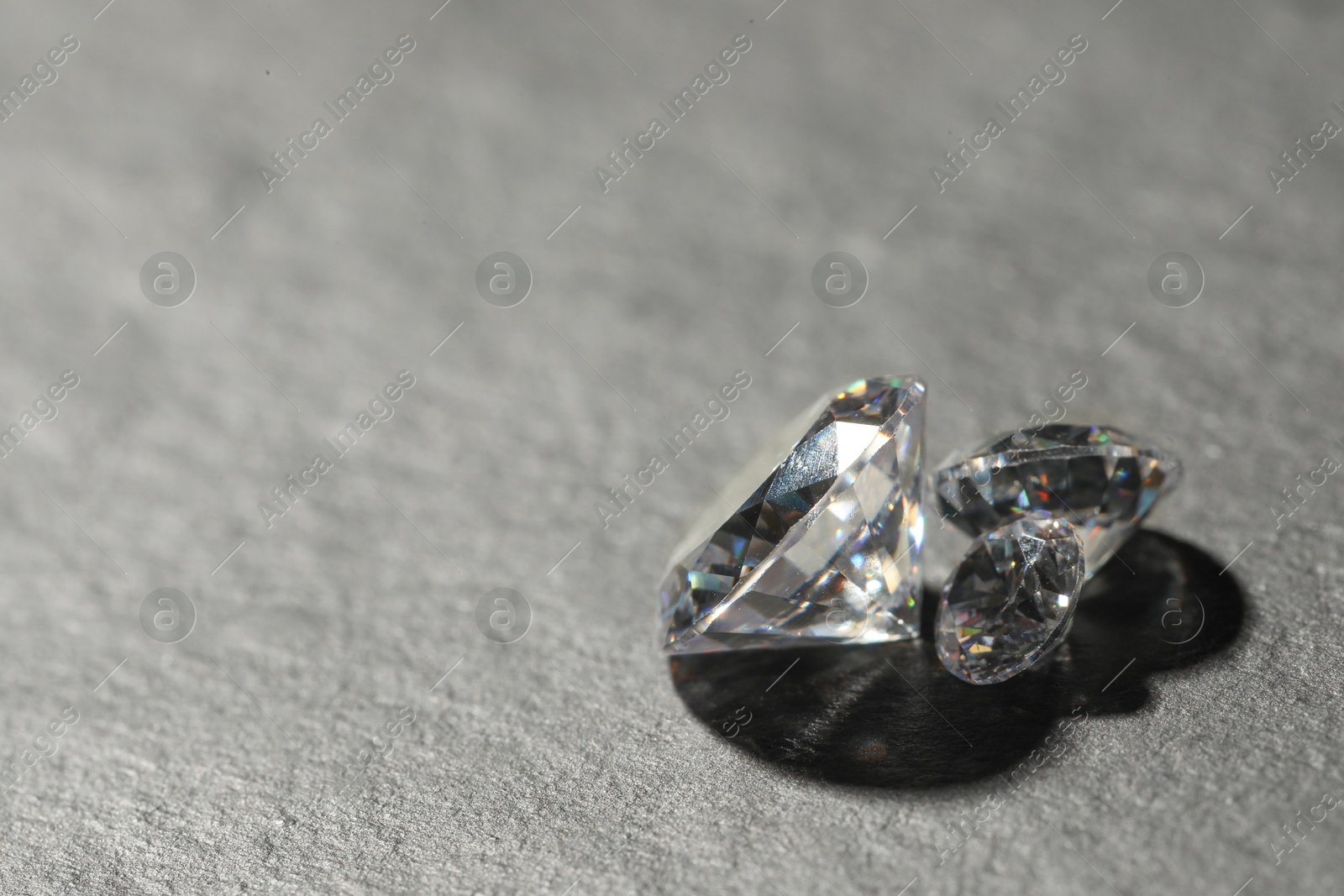 Photo of Beautiful shiny diamonds on grey table, closeup. Space for text