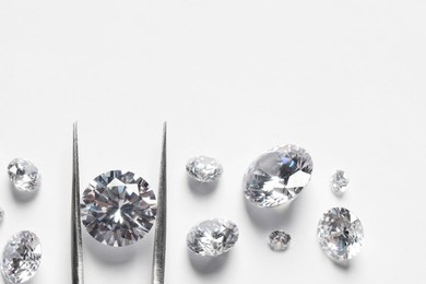 Many beautiful shiny diamonds and tweezers on white background, flat lay. Space for text