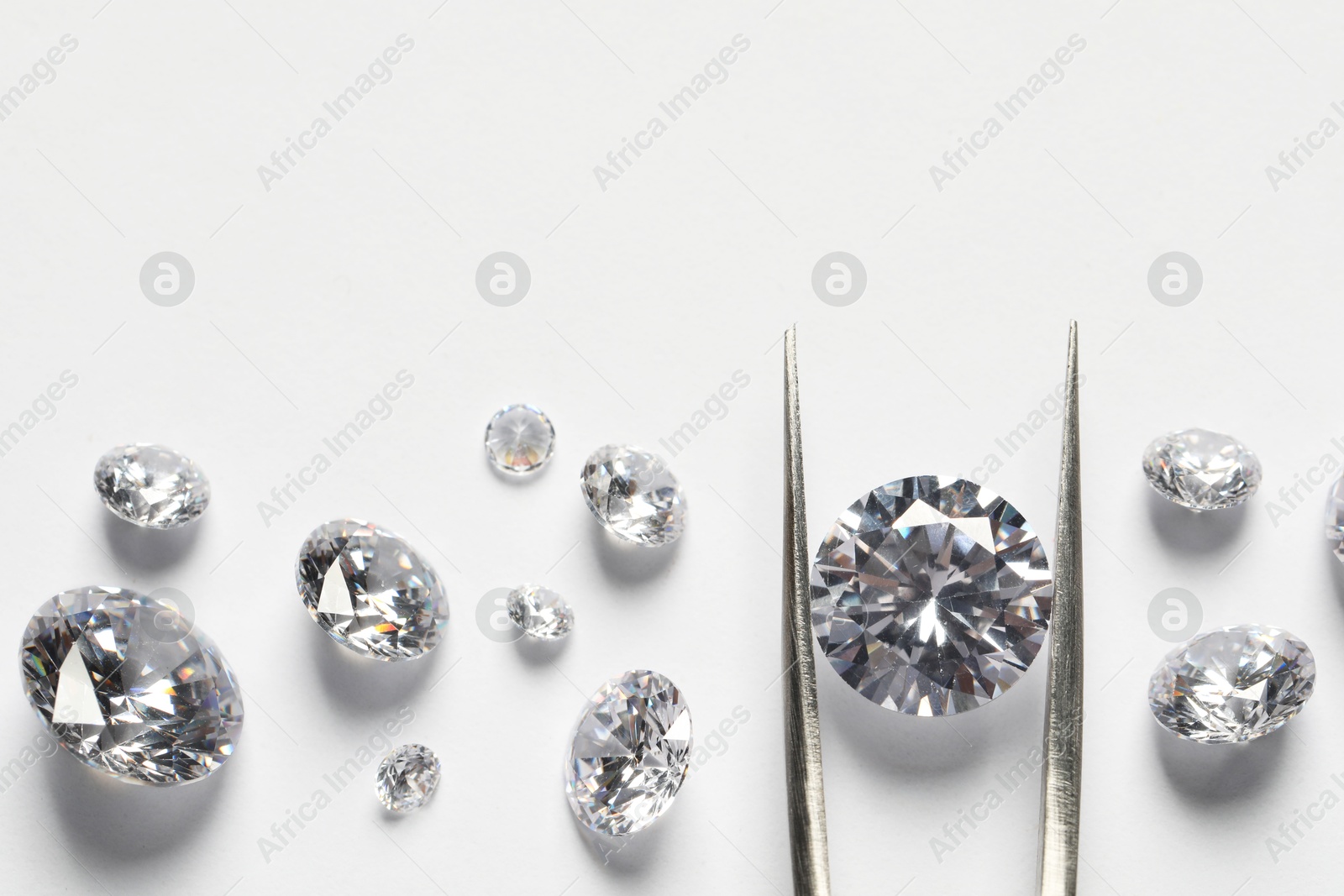 Photo of Many beautiful shiny diamonds and tweezers on white background, flat lay. Space for text