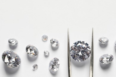 Photo of Many beautiful shiny diamonds and tweezers on white background, flat lay. Space for text