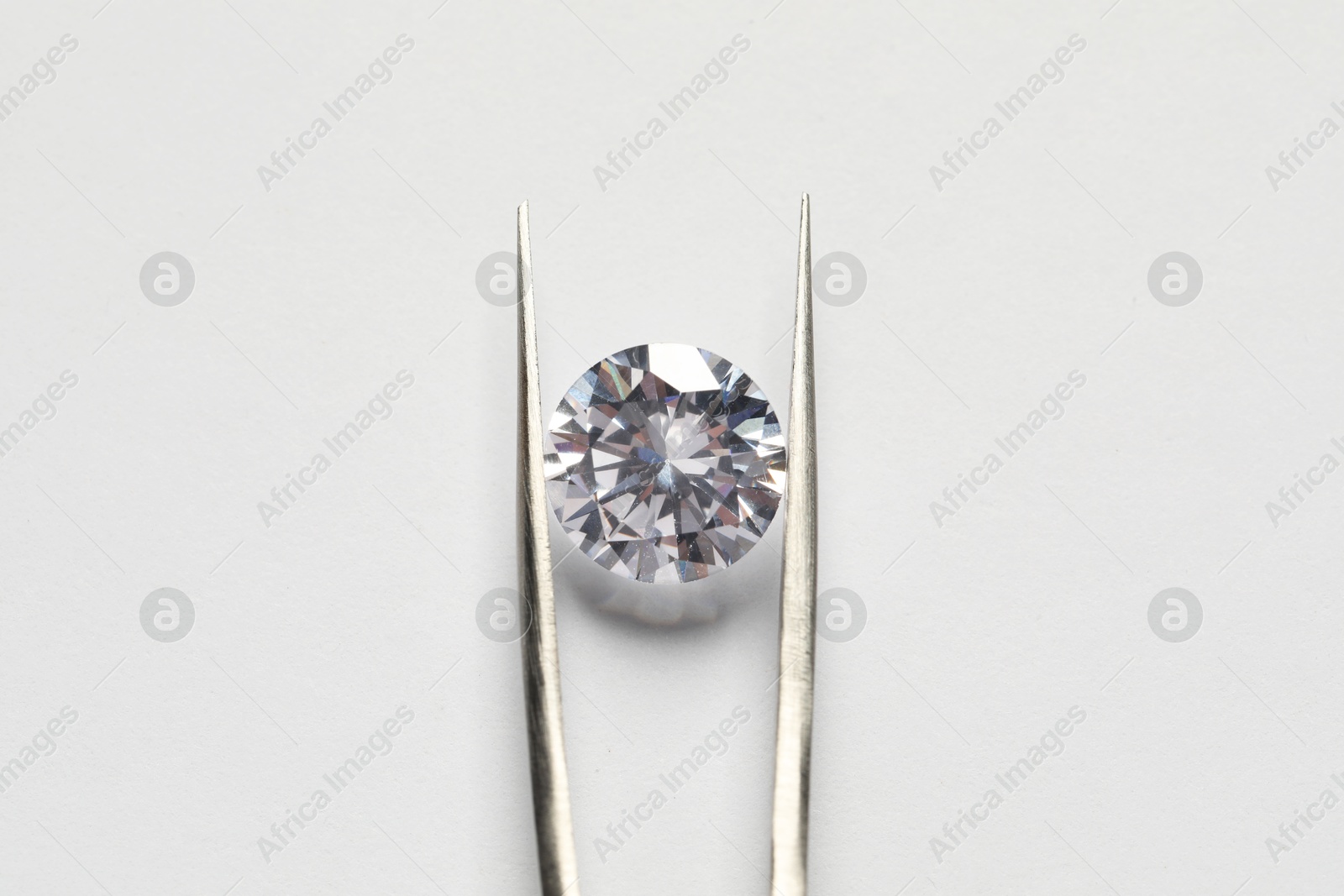 Photo of Beautiful shiny diamond and tweezers on white background, top view