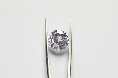 Photo of Beautiful shiny diamond and tweezers on white background, top view