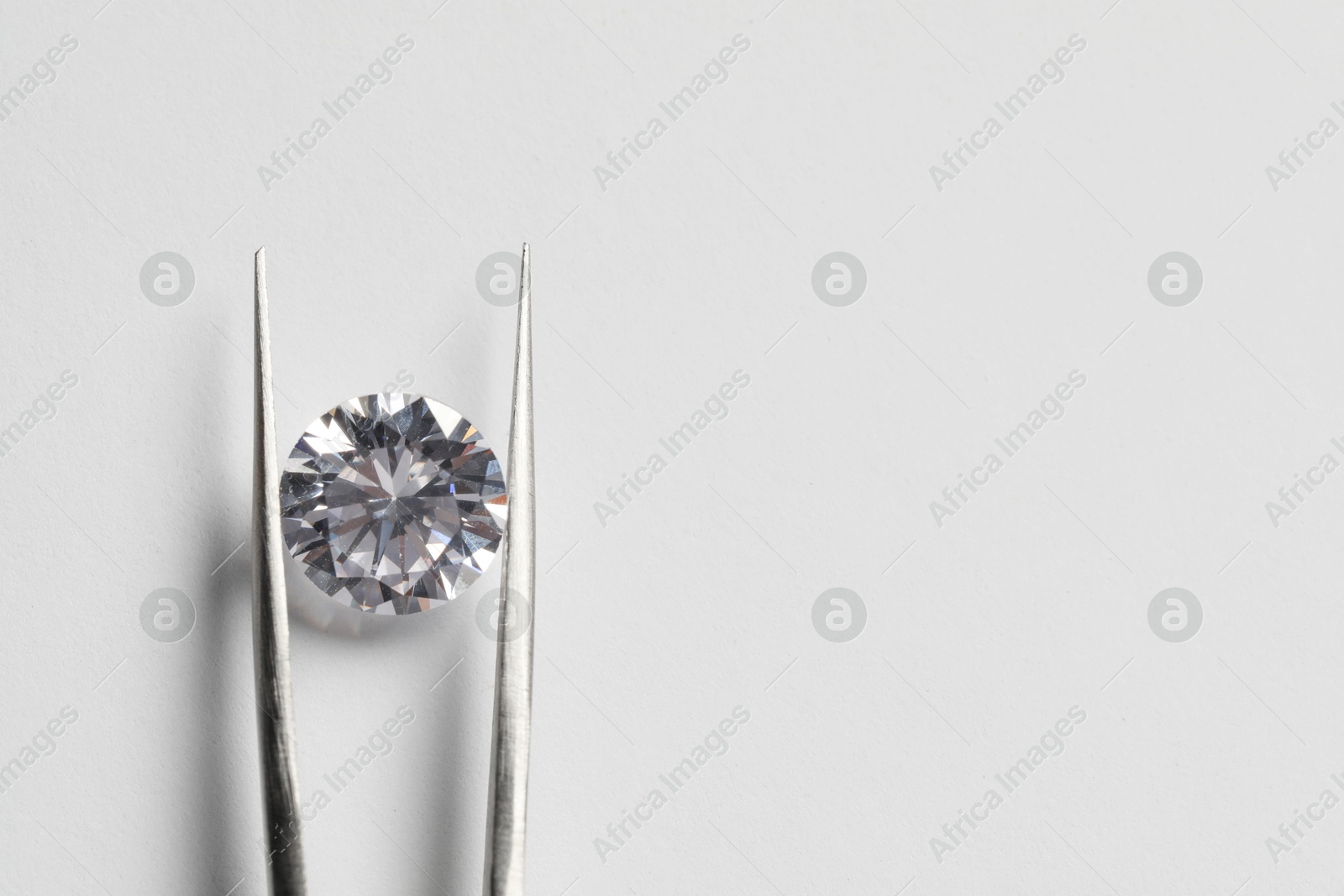 Photo of Beautiful shiny diamond and tweezers on white background, top view. Space for text