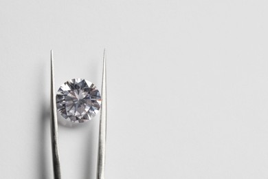 Photo of Beautiful shiny diamond and tweezers on white background, top view. Space for text