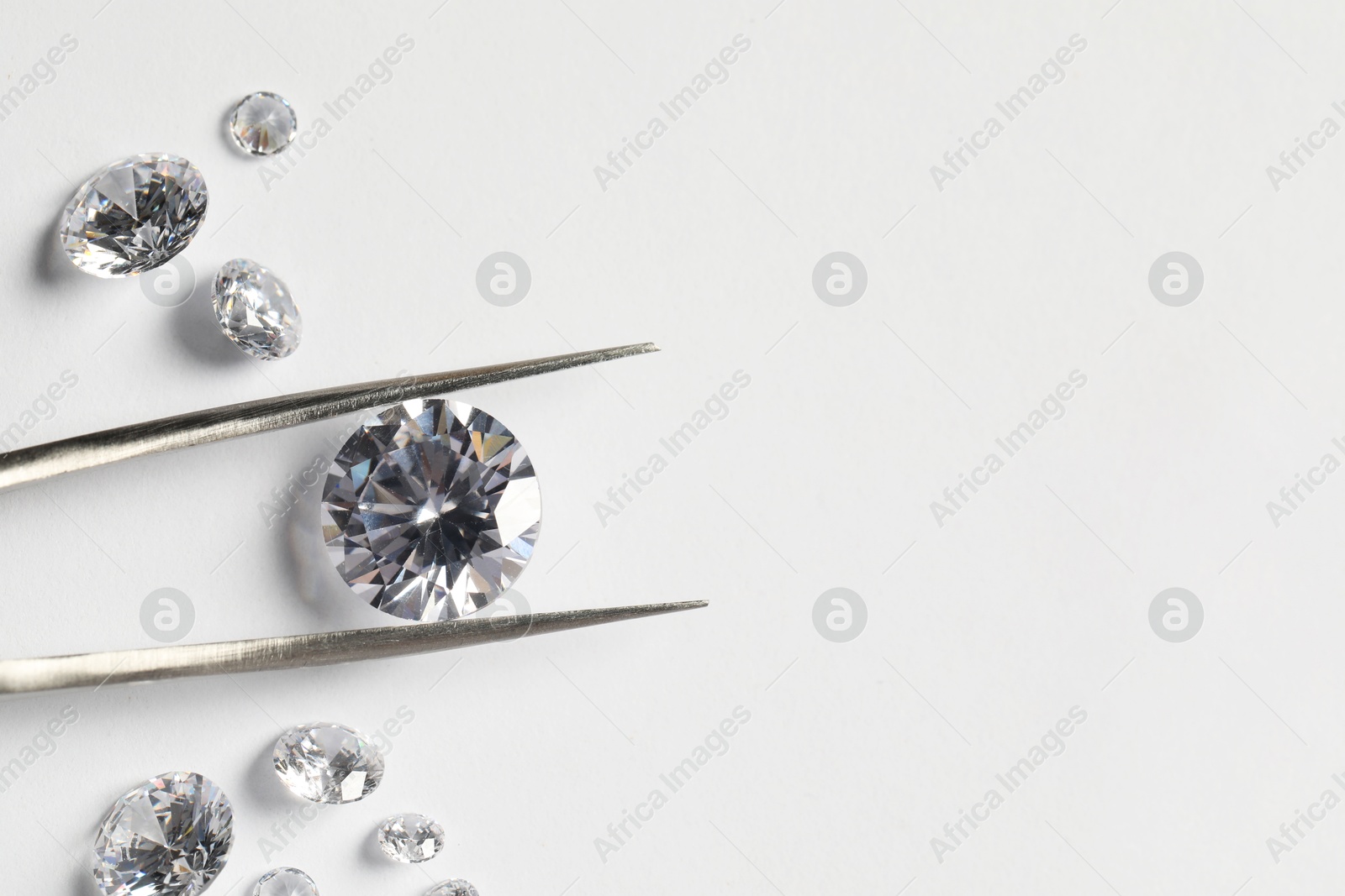 Photo of Many beautiful shiny diamonds and tweezers on white background, flat lay. Space for text