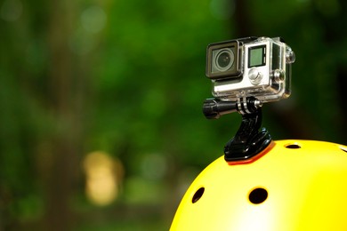 Modern action camera with mount on helmet outdoors, closeup. Space for text