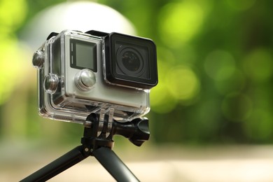 Photo of Modern action camera with tripod outdoors, closeup. Space for text