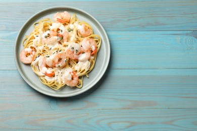 Photo of Delicious pasta with shrimps on blue wooden table, top view. Space for text