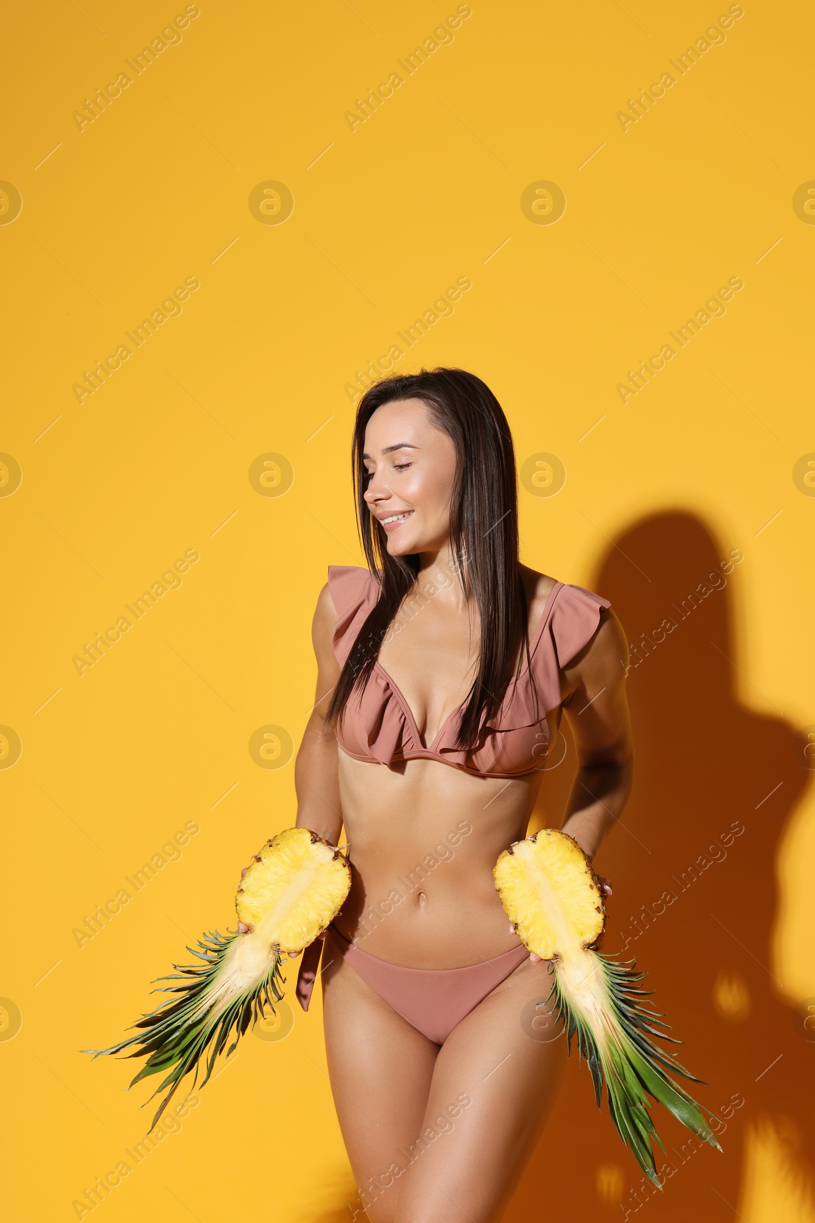 Photo of Attractive woman in bikini with halves of pineapple on orange background