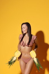 Photo of Attractive woman in bikini with halves of pineapple on orange background