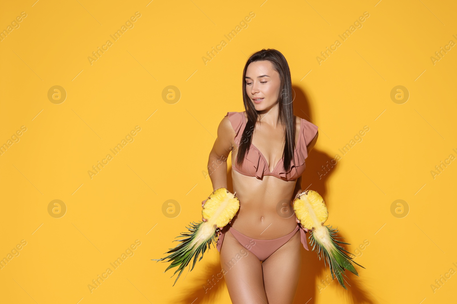 Photo of Attractive woman in bikini with halves of pineapple on orange background, space for text